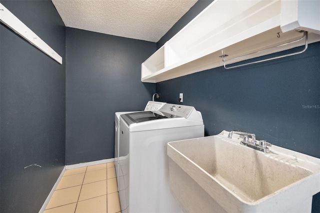 laundry room featuring washer and clothes dryer, a textured ceiling, light tile patterned floors, and baseboards