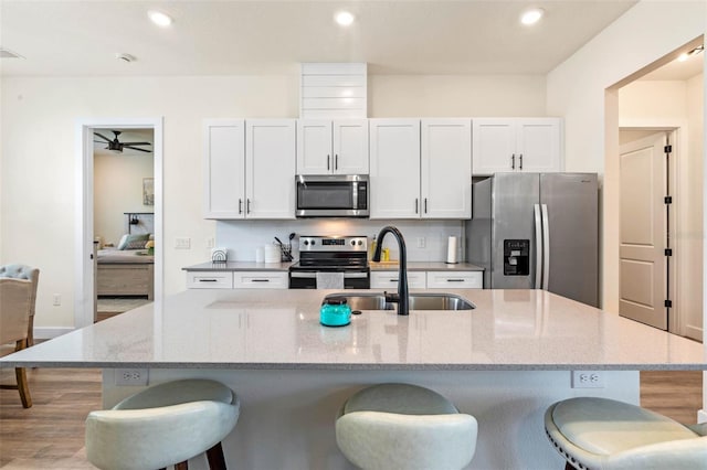 kitchen with stainless steel appliances, a sink, a kitchen breakfast bar, a kitchen island with sink, and a ceiling fan