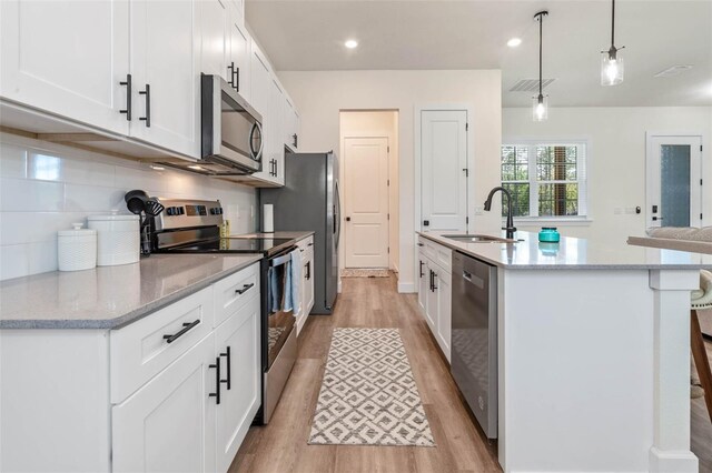 kitchen with stainless steel appliances, a sink, light wood-style floors, a center island with sink, and recessed lighting