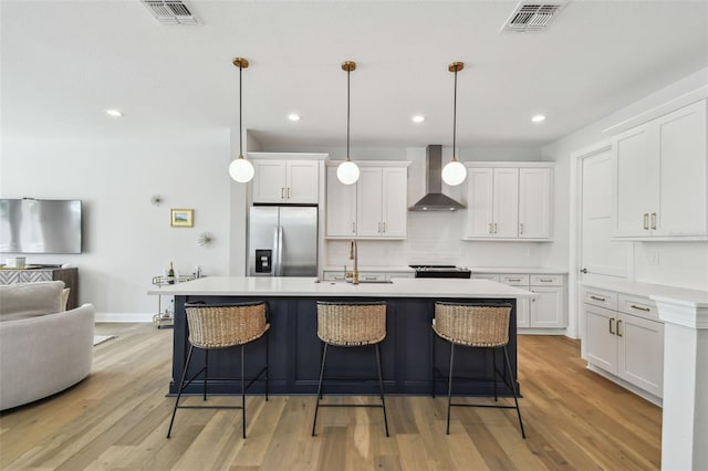 kitchen featuring stainless steel fridge with ice dispenser, wall chimney range hood, a sink, a kitchen breakfast bar, and recessed lighting