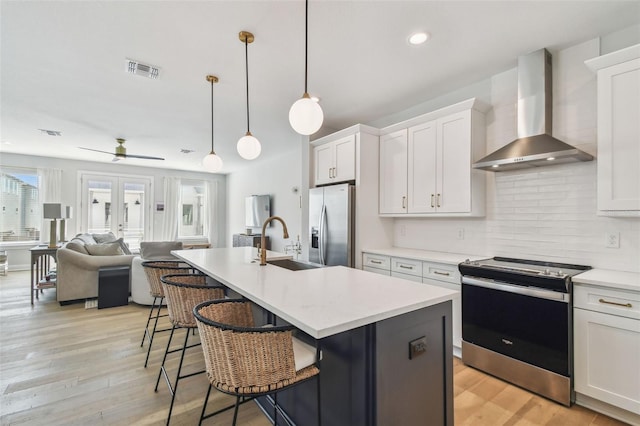 kitchen featuring appliances with stainless steel finishes, wall chimney exhaust hood, a sink, open floor plan, and white cabinetry