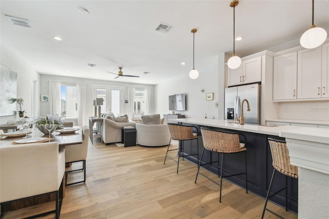 kitchen featuring stainless steel fridge, a breakfast bar area, light countertops, a ceiling fan, and light wood-style floors