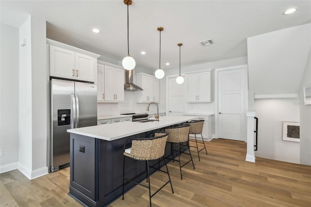 kitchen with stainless steel appliances, wall chimney range hood, white cabinetry, light wood-style flooring, and recessed lighting