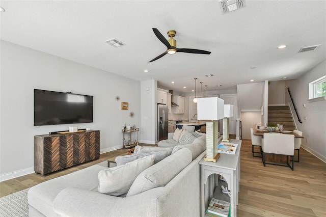 living area with light wood-style flooring, ceiling fan, stairs, baseboards, and recessed lighting