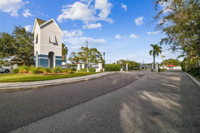 view of asphalt street featuring sidewalks, curbs, a gate, and a gated entry