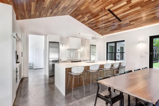 kitchen with built in fridge, wooden ceiling, white cabinets, light countertops, and a kitchen breakfast bar