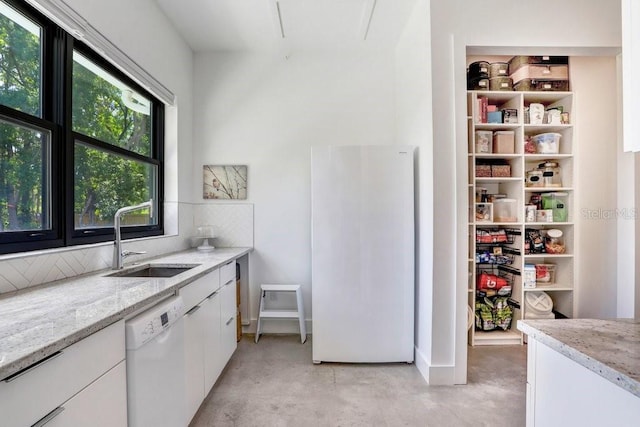 kitchen with white appliances, a sink, concrete floors, white cabinetry, and light stone counters