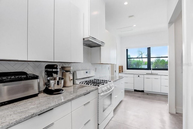 kitchen featuring white gas range, white cabinetry, decorative backsplash, light stone counters, and finished concrete floors