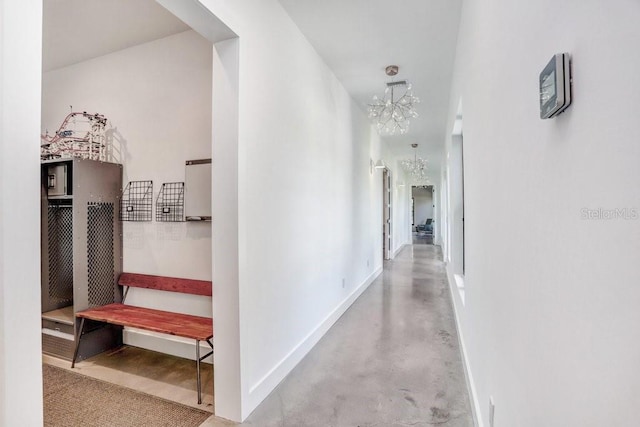 hallway featuring a chandelier, baseboards, and finished concrete floors