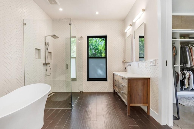 bathroom featuring a shower stall, vanity, wood finished floors, a walk in closet, and a freestanding tub