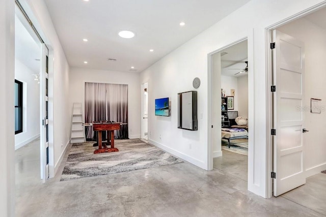 hall featuring concrete floors, baseboards, and recessed lighting