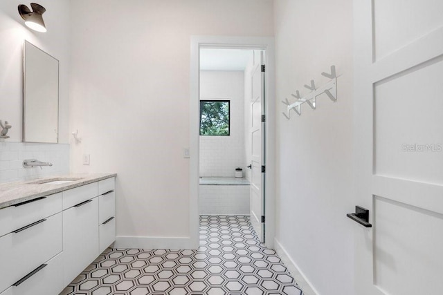 bathroom featuring baseboards, vanity, tile patterned floors, tasteful backsplash, and a bath