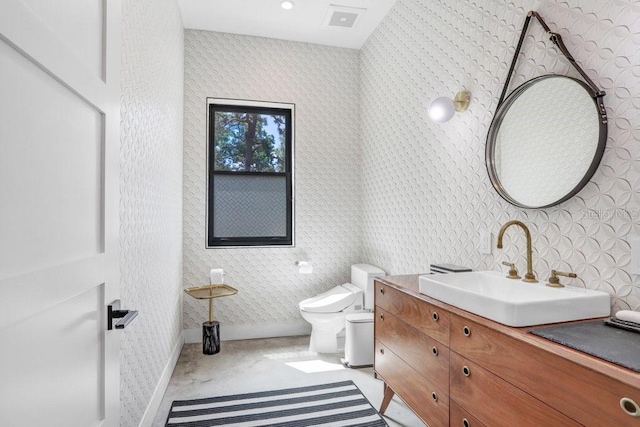 bathroom with wallpapered walls, toilet, vanity, and baseboards