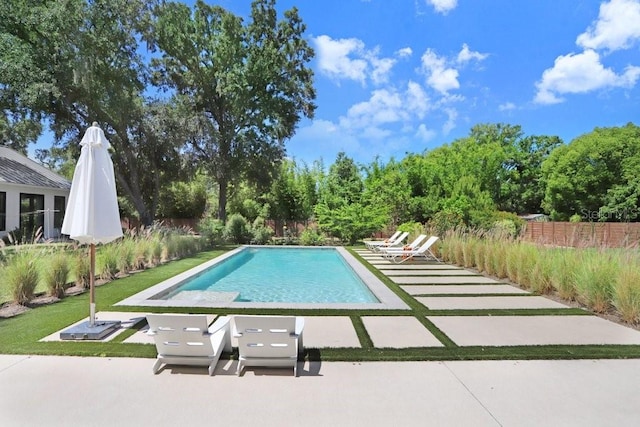 view of swimming pool featuring fence, a patio area, and view of wooded area