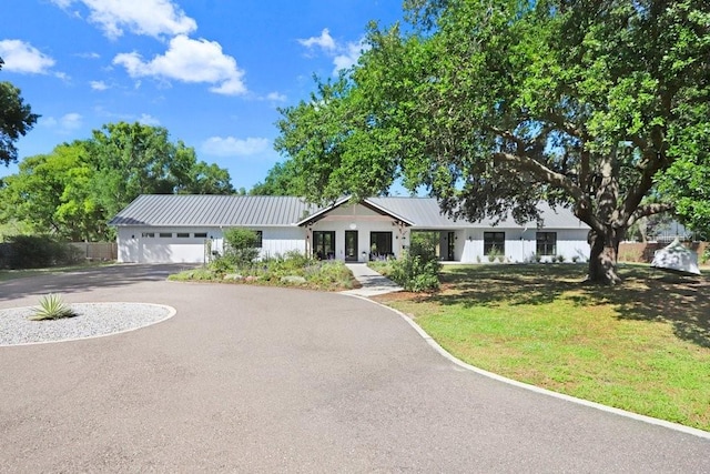 view of front of house with driveway, a front lawn, metal roof, and an attached garage