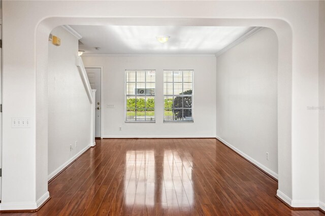 empty room with arched walkways, crown molding, wood finished floors, baseboards, and stairway