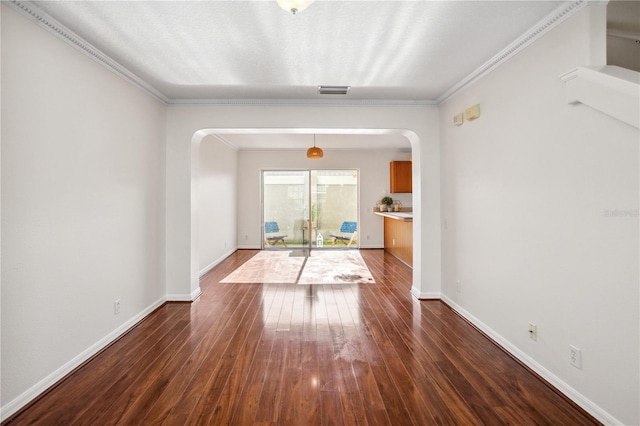 empty room featuring arched walkways, dark wood finished floors, baseboards, and ornamental molding