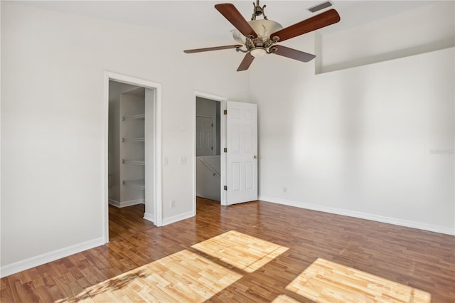 unfurnished bedroom with a spacious closet, wood finished floors, baseboards, a closet, and a ceiling fan