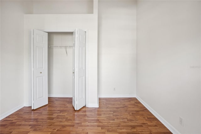 unfurnished bedroom featuring wood finished floors, baseboards, and a closet