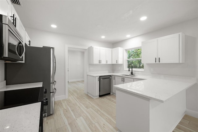 2157 20th Ave SW, Largo, FL 33774 - kitchen featuring appliances with stainless steel finishes, a sink, a peninsula, light wood finished floors, and white cabinets