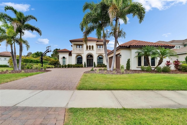 mediterranean / spanish house with decorative driveway, a balcony, stucco siding, a garage, and a front lawn