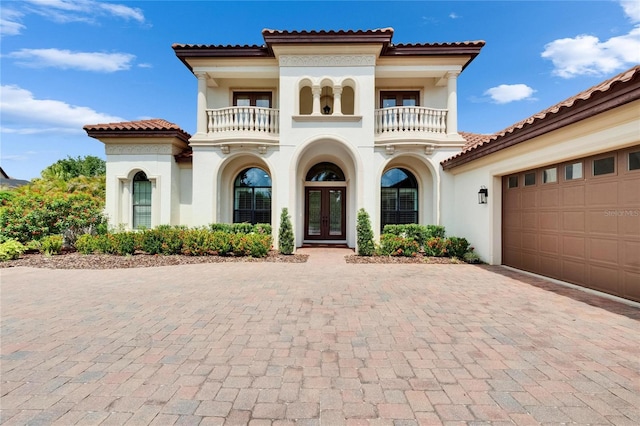 mediterranean / spanish house featuring french doors, a balcony, stucco siding, decorative driveway, and a garage
