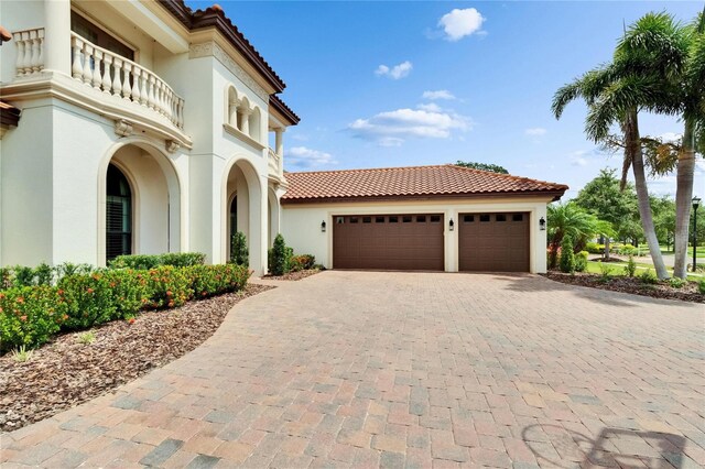 mediterranean / spanish house with stucco siding, decorative driveway, a tile roof, an attached garage, and a balcony
