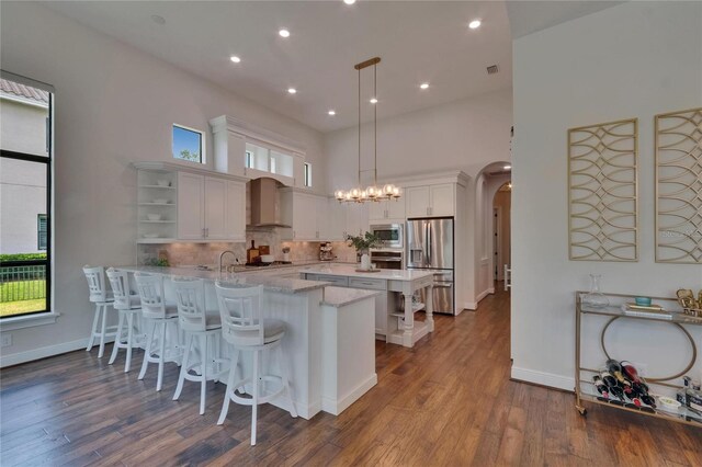 kitchen featuring open shelves, appliances with stainless steel finishes, arched walkways, a peninsula, and wall chimney exhaust hood