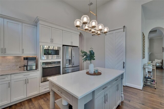 kitchen with appliances with stainless steel finishes, arched walkways, light countertops, decorative backsplash, and dark wood finished floors