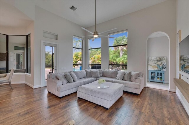 living room featuring dark wood-style flooring, a ceiling fan, a high ceiling, and baseboards