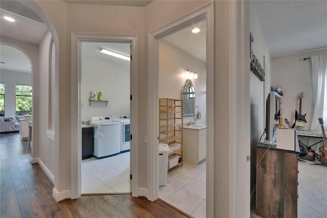 hallway with independent washer and dryer, arched walkways, light wood-type flooring, and a sink