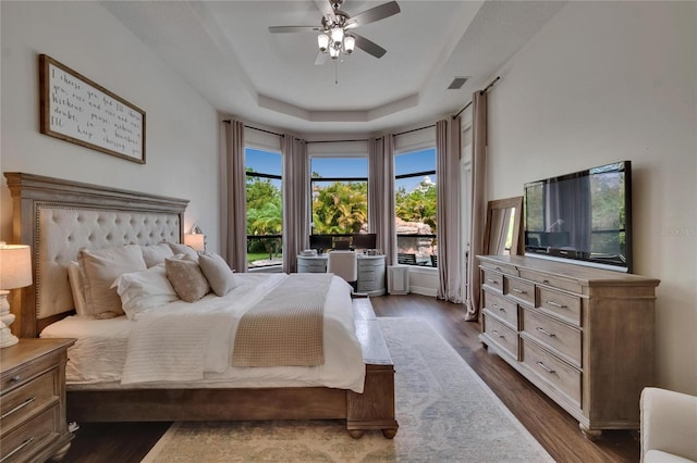 bedroom with a raised ceiling, dark wood-style floors, and ceiling fan