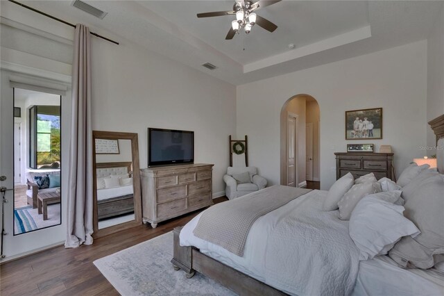 bedroom with arched walkways, dark wood-style floors, a tray ceiling, and a ceiling fan