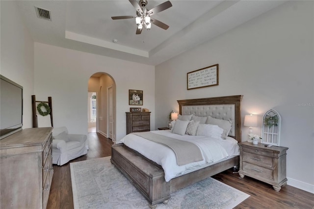 bedroom with arched walkways, dark wood-style floors, a raised ceiling, baseboards, and ceiling fan