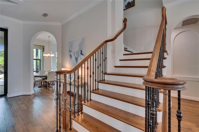 stairs with arched walkways, wood finished floors, baseboards, ornamental molding, and a chandelier