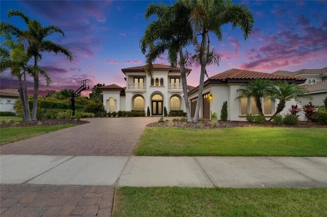 mediterranean / spanish house featuring decorative driveway, an attached garage, stucco siding, a tile roof, and a front lawn