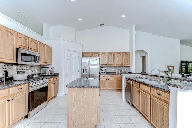 7107 Colonial Lake Dr, Riverview, FL 33578 - kitchen featuring appliances with stainless steel finishes, an island with sink, light brown cabinetry, arched walkways, and high vaulted ceiling