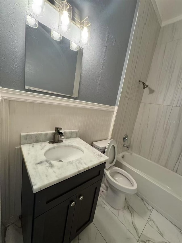 full bathroom with wainscoting, toilet, vanity, marble finish flooring, and washtub / shower combination