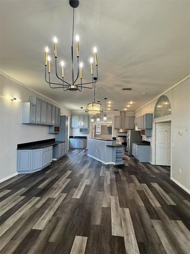 kitchen with dark countertops, freestanding refrigerator, crown molding, a chandelier, and dark wood-type flooring