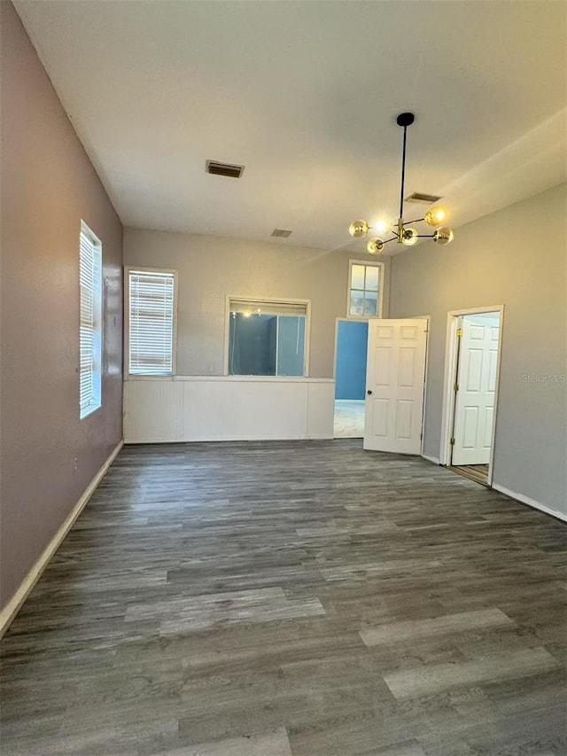 spare room featuring a chandelier, plenty of natural light, wood finished floors, and baseboards