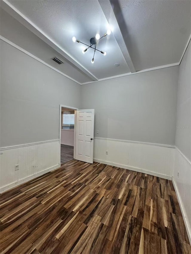 empty room with a chandelier, wood finished floors, a wainscoted wall, and a textured ceiling