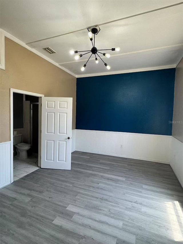 unfurnished room featuring a chandelier, wainscoting, wood finished floors, and crown molding