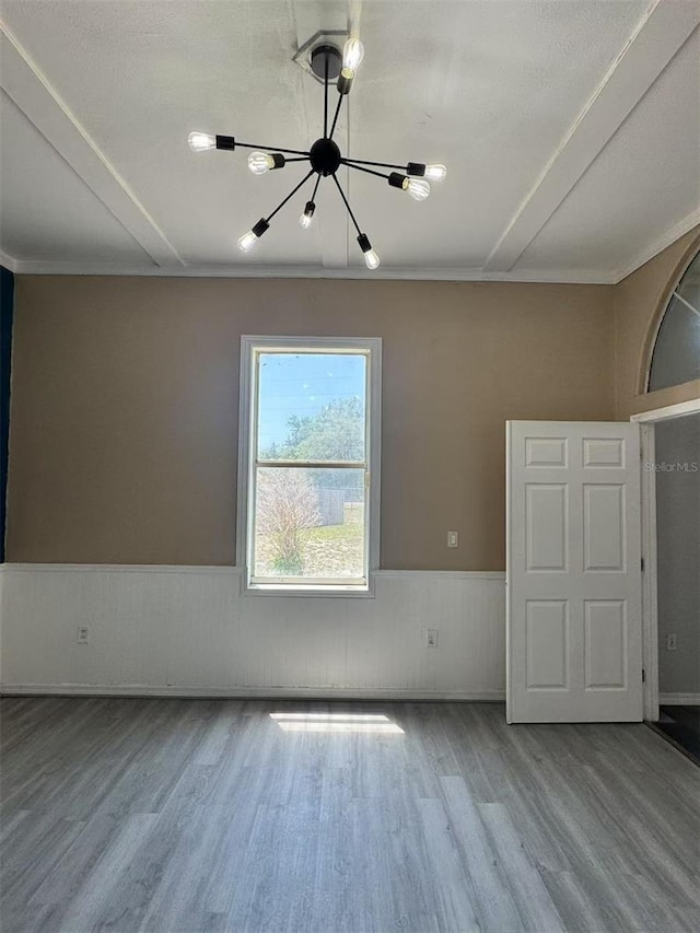 unfurnished room featuring a chandelier, wood finished floors, and a wainscoted wall