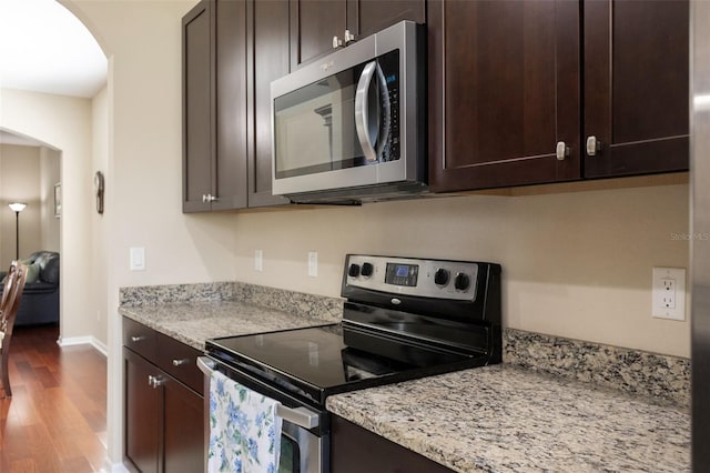 10837 Breaking Rocks Dr, Tampa, FL 33647 - kitchen featuring appliances with stainless steel finishes, arched walkways, wood finished floors, dark brown cabinets, and light stone counters