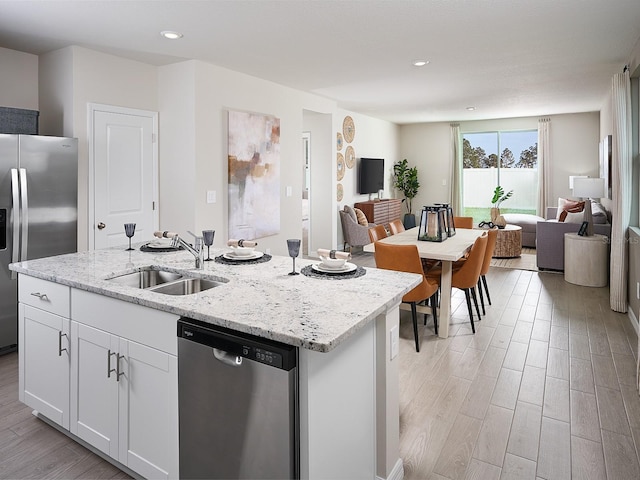 kitchen featuring appliances with stainless steel finishes, open floor plan, a sink, a center island with sink, and light wood finished floors