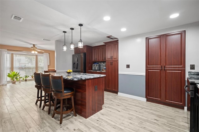 3413 W Kirby St, Tampa, FL 33614 - kitchen with stainless steel refrigerator with ice dispenser, a breakfast bar, a center island, reddish brown cabinets, and stone counters