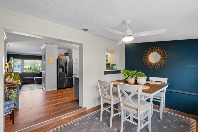 dining room with wood finished floors, a ceiling fan, baseboards, and a textured ceiling
