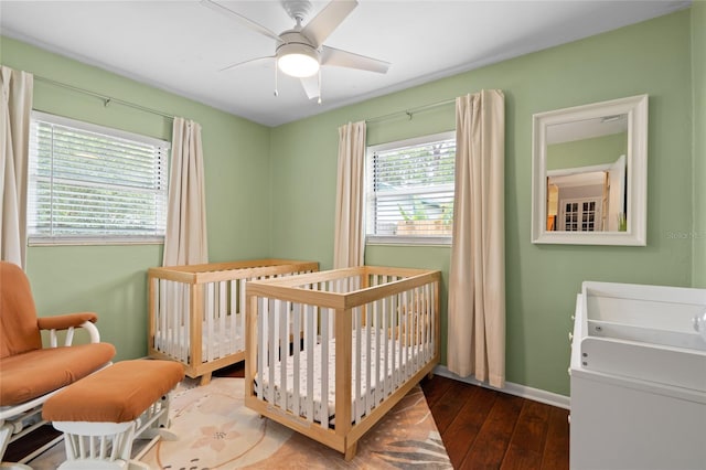 bedroom with wood-type flooring, a nursery area, baseboards, and a ceiling fan