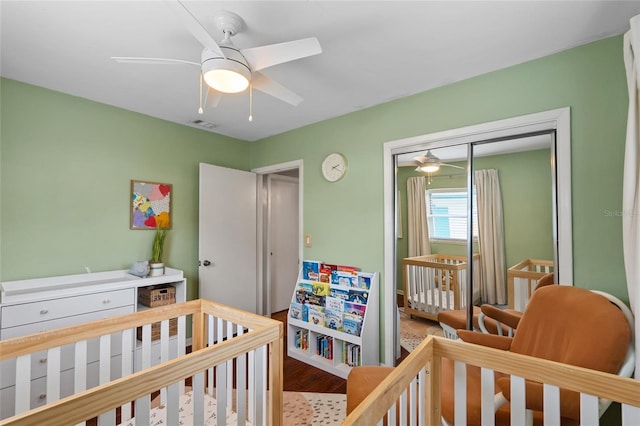 bedroom with wood finished floors, a crib, a closet, and a ceiling fan