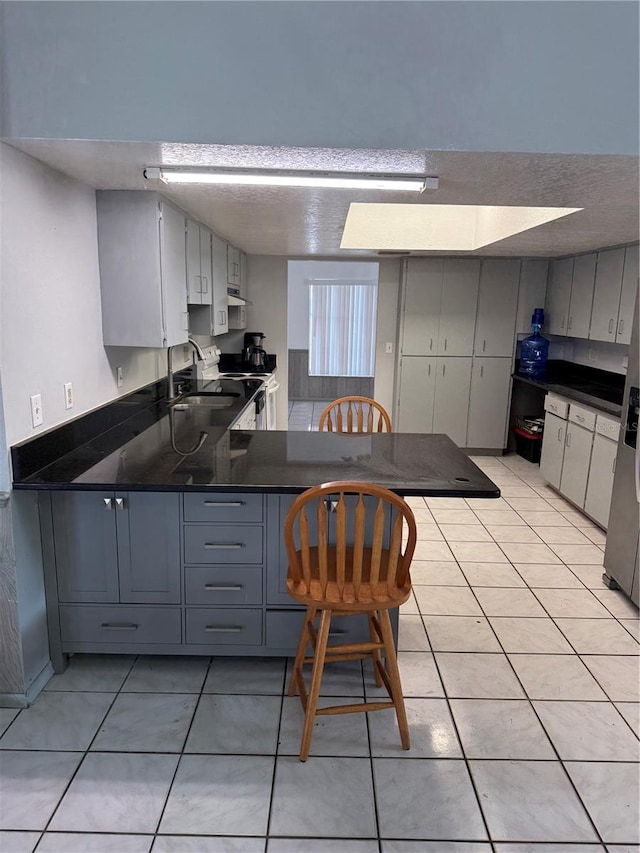 2026 Aaron Pl, Clearwater, FL 33760 - kitchen featuring gray cabinets, white electric range oven, light tile patterned floors, dark countertops, and a textured ceiling
